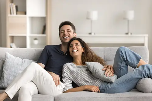Couple on sofa laughing Photo of a middle-aged couple relaxing on a sofa, laughing at a shared joke.